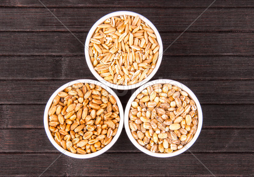 Пшеница, овсянка и перловка в круглых пиалках на темном фоне