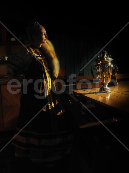 Девушка в русском сарафане в домашнем интерьере с самоваром