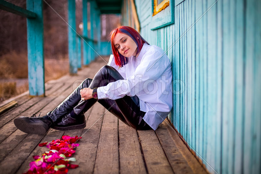 Девушка сидит на деревянном настиле, обхватив руками ногу