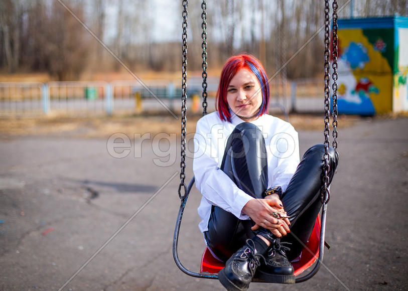 Девушка сидит на качелях, обнимая свои колени