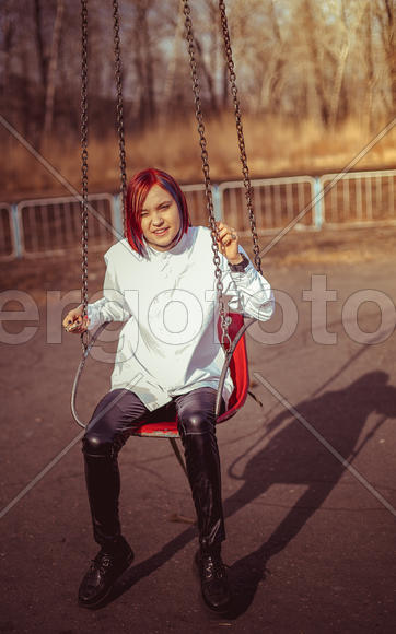 Девушка сидит на качелях и щурится от солнца