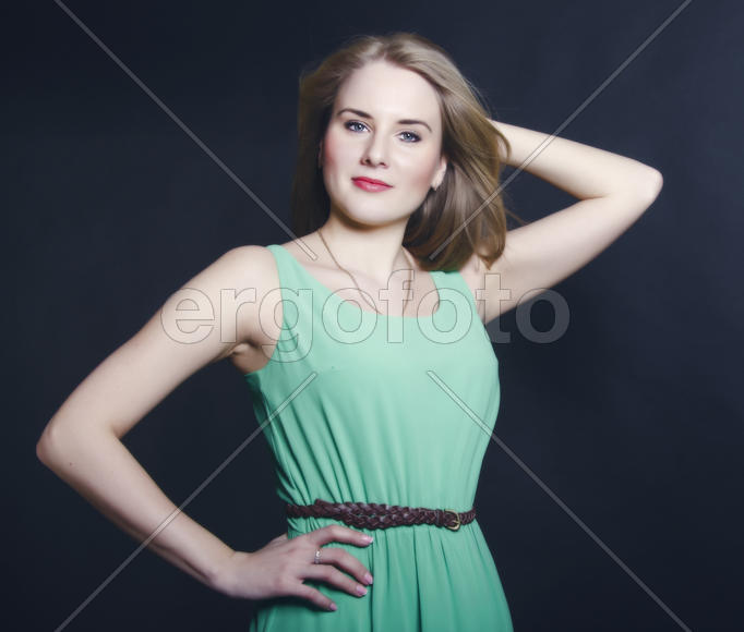 Beautiful blond girl with blue eyes in the green dress smiling on a dark