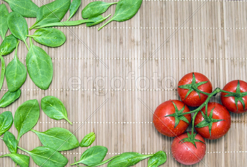 spinach leaves and branch of ripe tomatoes on a bamboo mat