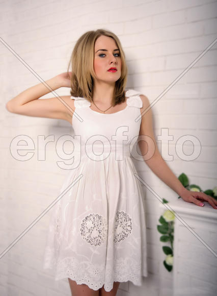 Beautiful blond girl with blue eyes in a white dress looks strictly on a white background