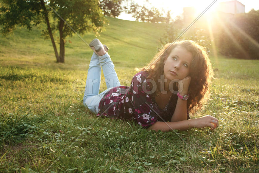 Девушка с длинными волосами в джинсах лежит на траве