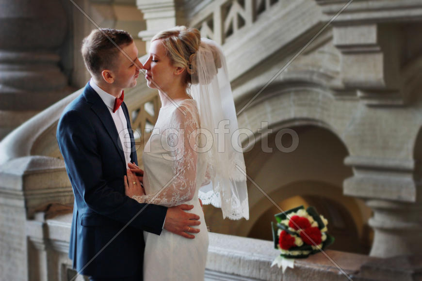 Жених и невеста обнимаются, сзади них них лежит миниатюрный букет невесты из красных и белых цветов 