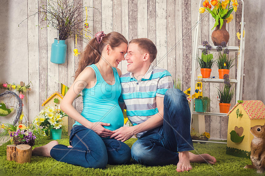 Беременная жена и муж сидят в окружении цветов и игрушек