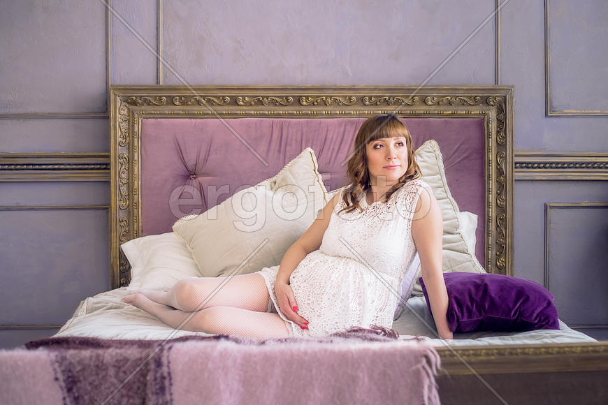 Беременная девушка в белом платье на постели