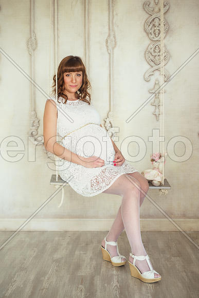 Беременная девушка в белом платье на качелях