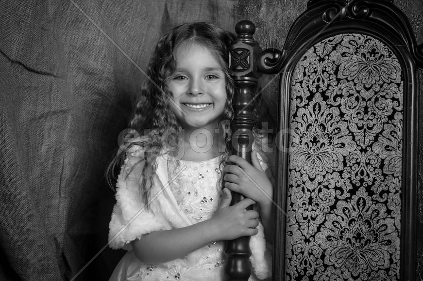 Улыбающаяся девочка стоит возле декоративного стулаа