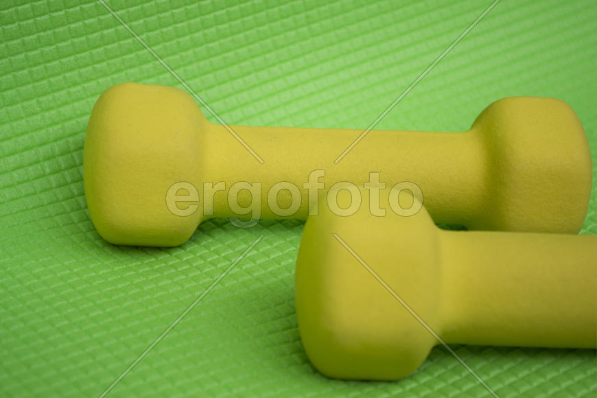 Жёлтые гантели на зелёном коврике