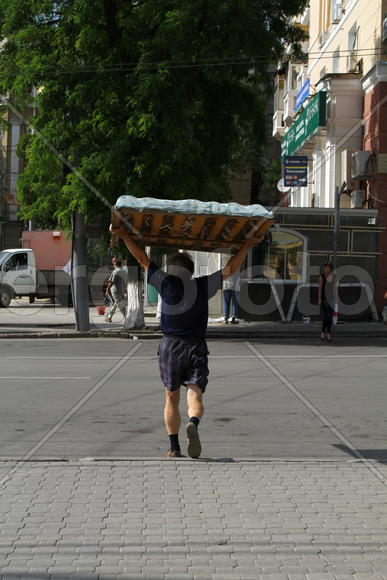 Мужчина несет над головой кровать 