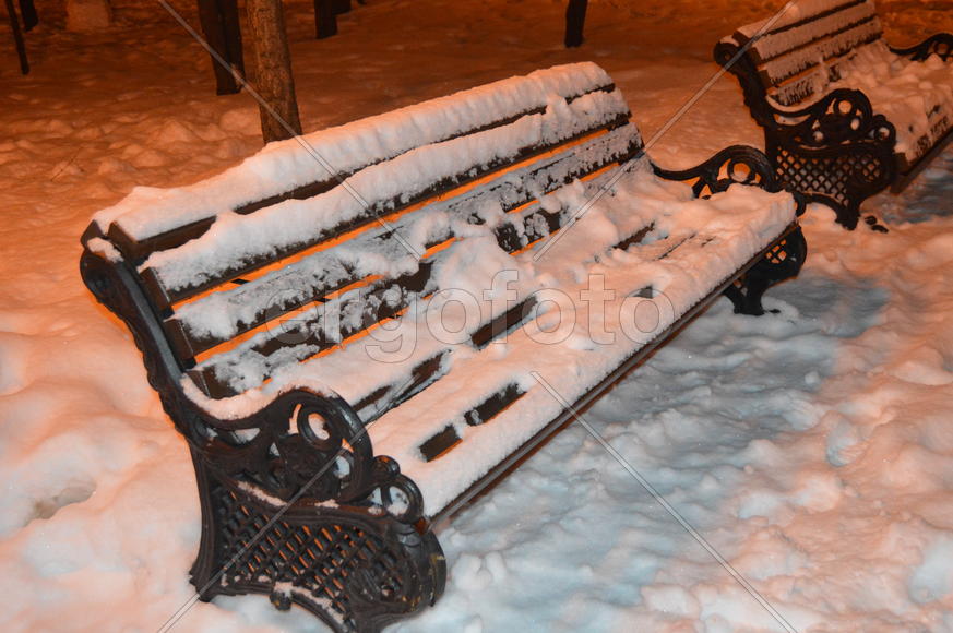 Занесенная снегом лавочка в парке 