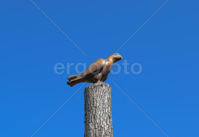 Фигурка Сокола на пне дерева напротив голубого неба.