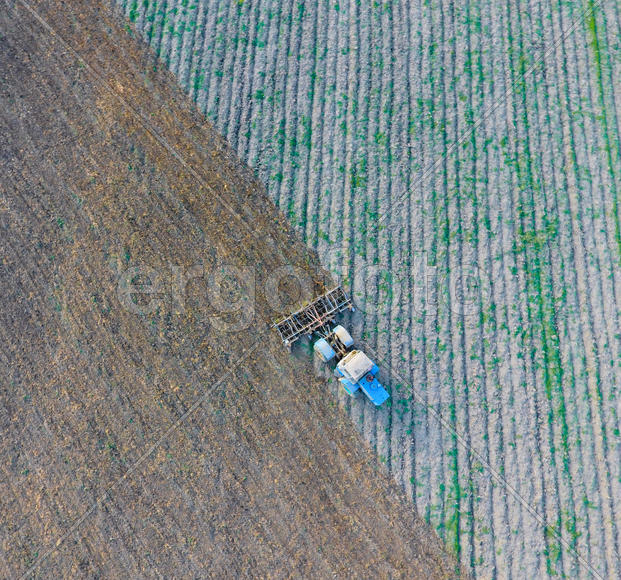 Вид сверху на трактор, который пашет поле. 