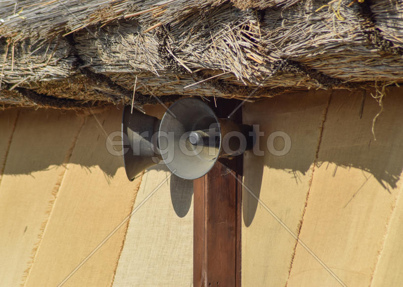 Винтажные рупорные громкоговорители на стене под соломенной крышей.