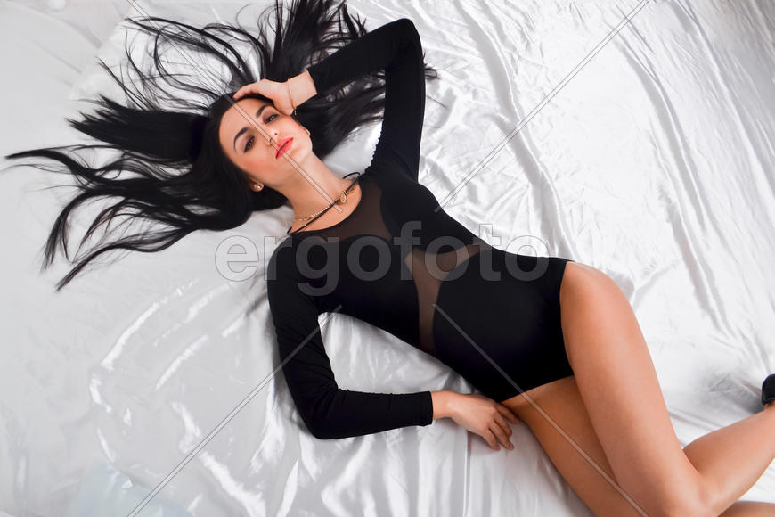 Девушка брюнетка в черном платье лежит на кровати