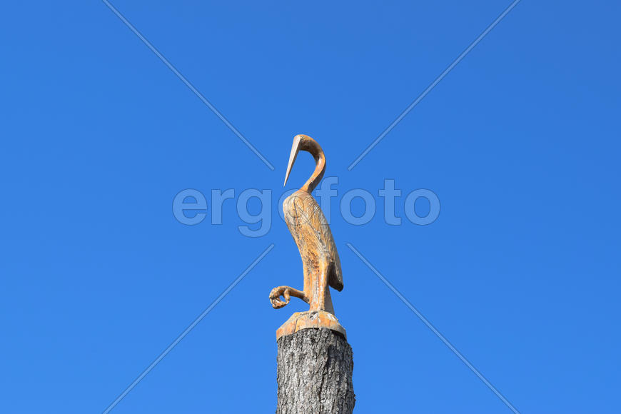 Фигурку журавлика на пне дерева напротив голубого неба.