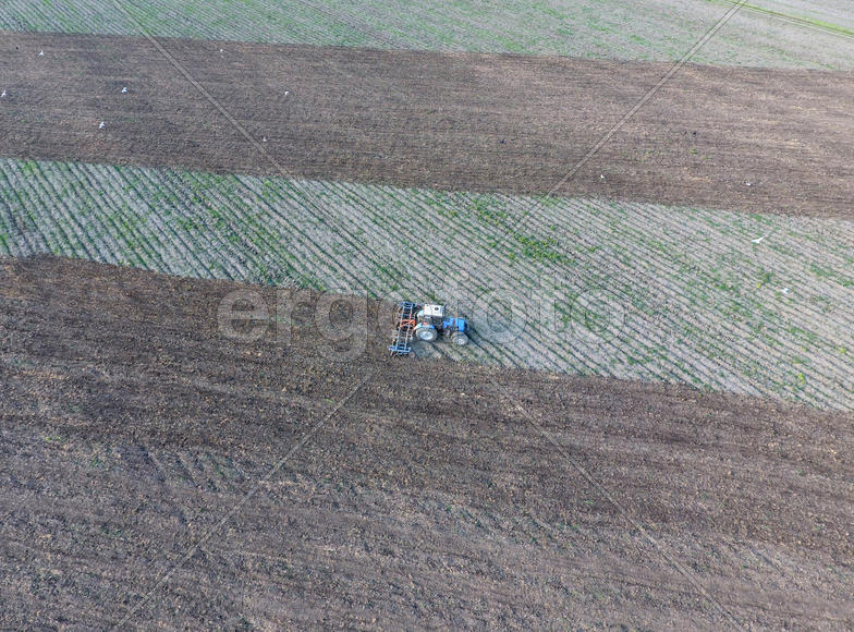 Вид сверху на трактор, который пашет поле. 