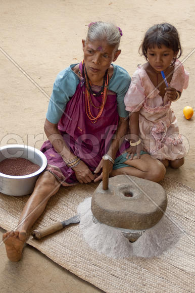 Grandmother and granddaughter make flour using a hand mill