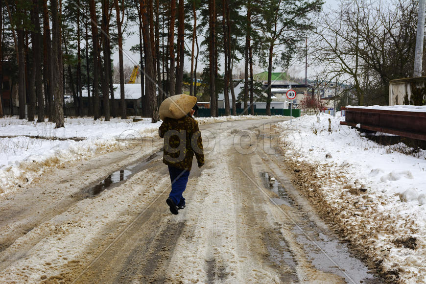 Человек несет большой мешок по дороге покрытой снегом 