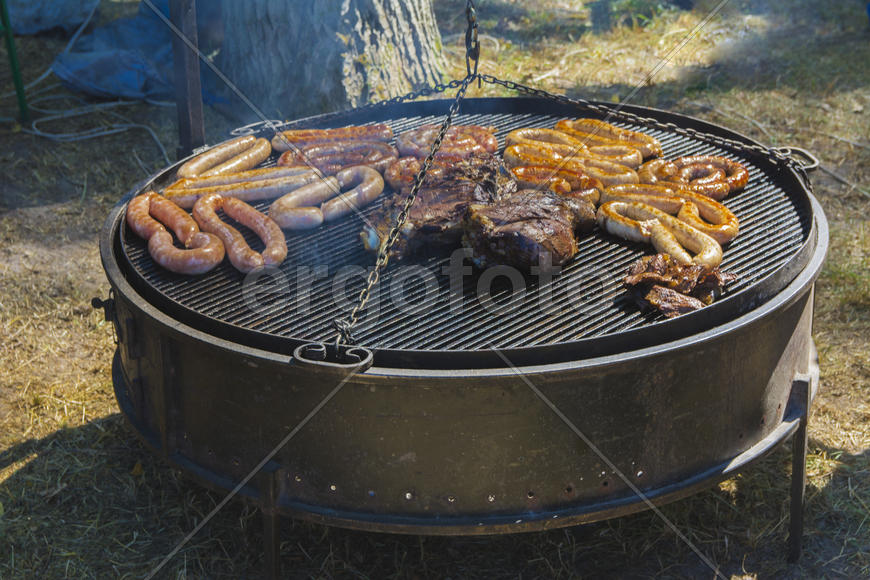 Roast large chunks of meat and sausage on a large grill