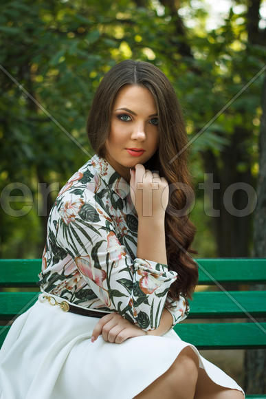 Beautiful brunette girl poses and relaxed on bench outdoors