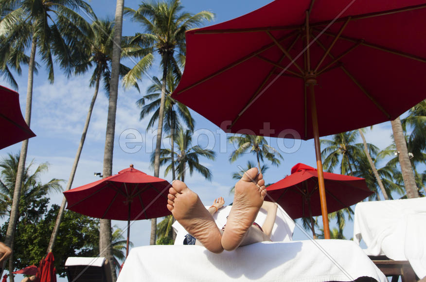 The person on vacation lies on a chaise lounge under an umbrella in beams of the tropical sun