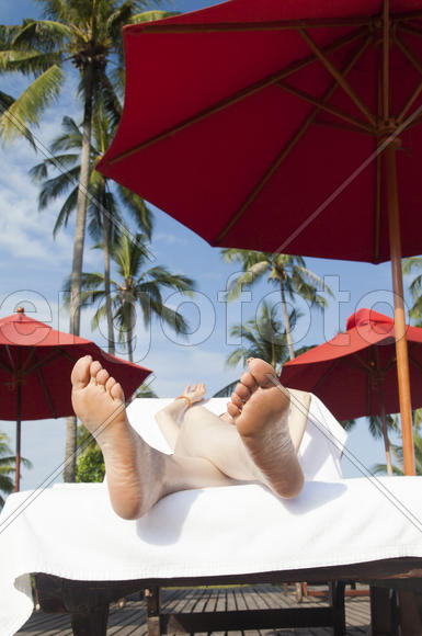 The person on vacation lies on a chaise lounge under an umbrella in beams of the tropical sun