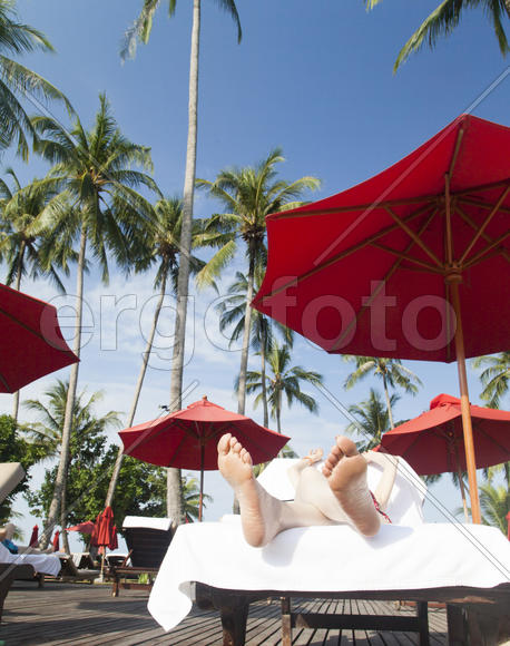 The person on vacation lies on a chaise lounge under an umbrella in beams of the tropical sun