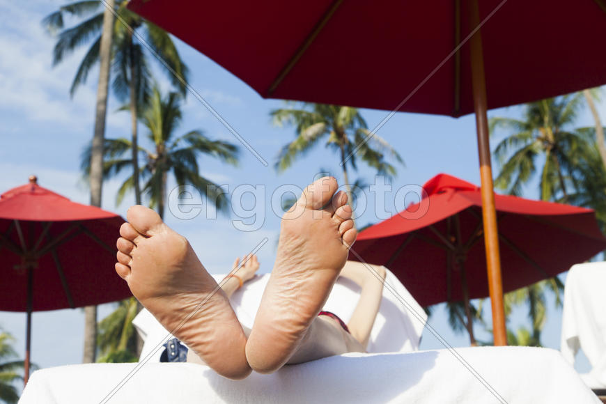 The person on vacation lies on a chaise lounge under an umbrella in beams of the tropical sun