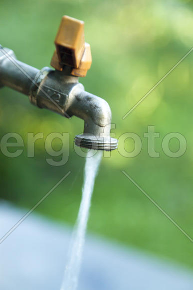The water tap is opened and water flows out of it in the background of nature