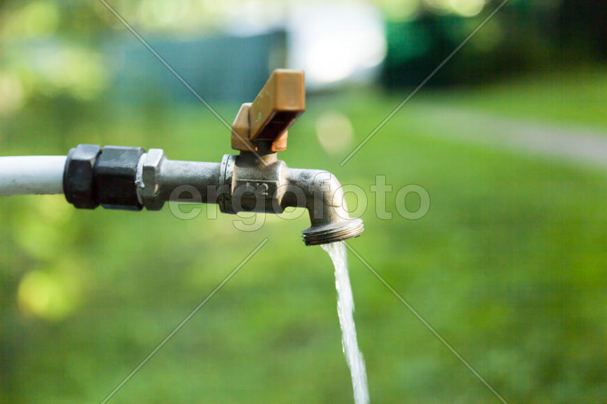 The water tap is opened and water flows out of it in the background of nature