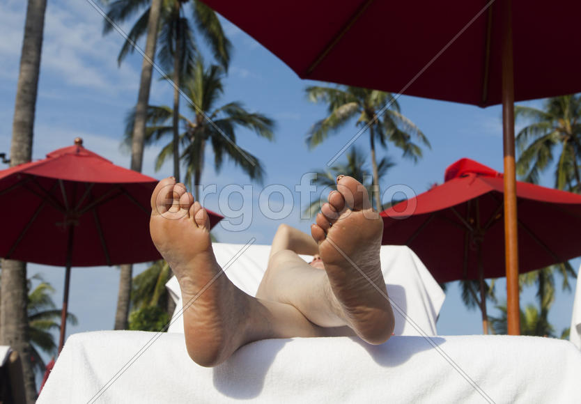 The person on vacation lies on a chaise lounge under an umbrella in beams of the tropical sun