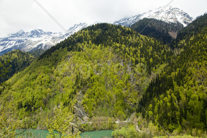 Mountains are covered with snow and the wood and surrounded with clouds