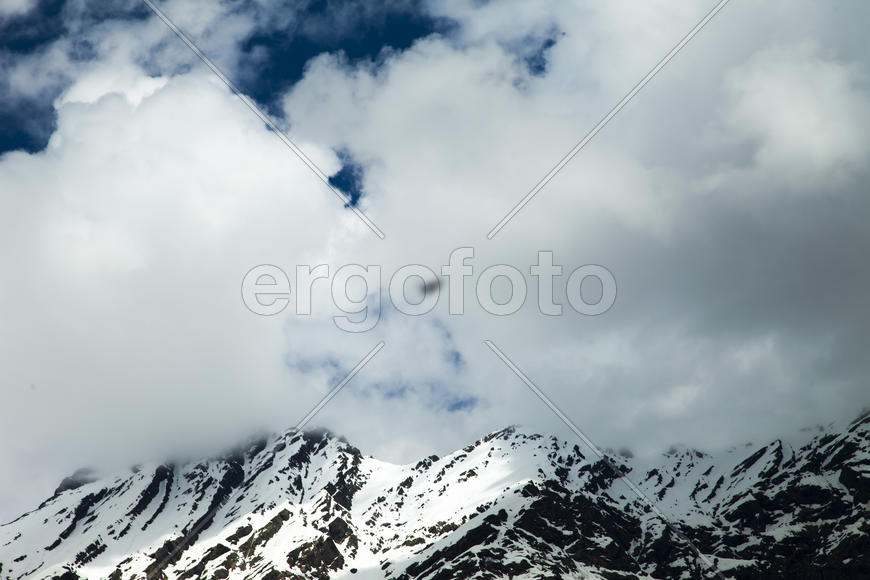 Mountains are covered with snow and the wood and surrounded with clouds