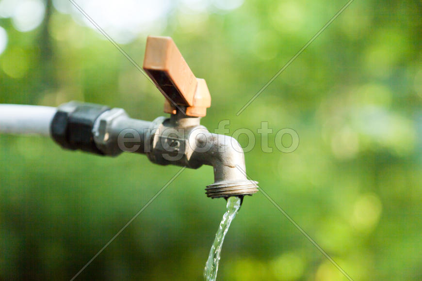 The water tap is opened and water flows out of it in the background of nature