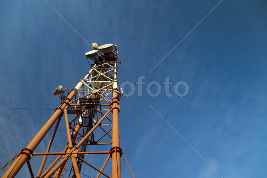 Communication tower against the bright blue sky with clouds