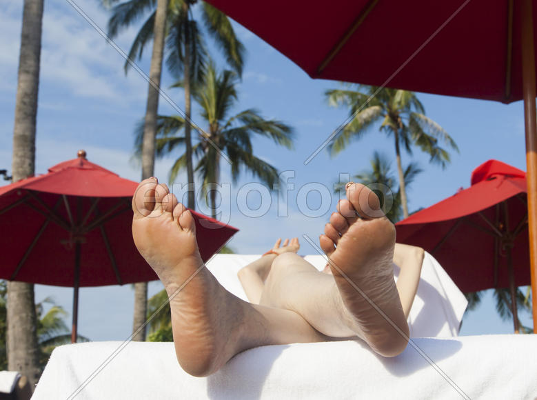 The person on vacation lies on a chaise lounge under an umbrella in beams of the tropical sun