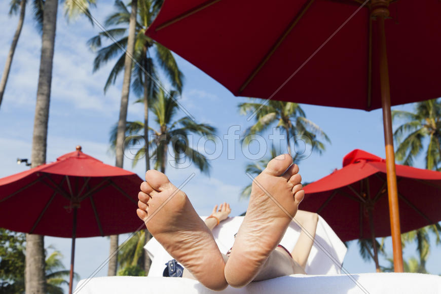 The person on vacation lies on a chaise lounge under an umbrella in beams of the tropical sun