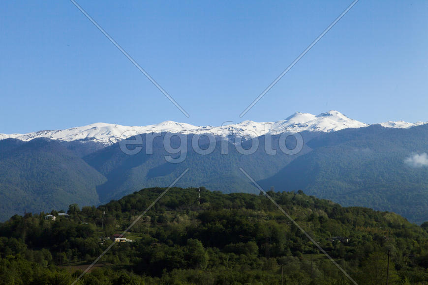 Mountains are covered with snow and the wood and surrounded with clouds