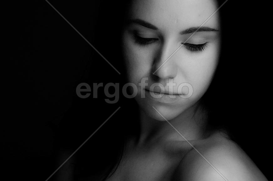 Темноволосая девушка стоит в полоборота и задумчиво смотрит вниз