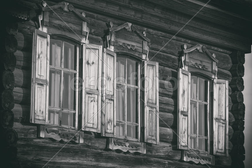 Три окна бревенчатого дома с резными наличниками и ставнями