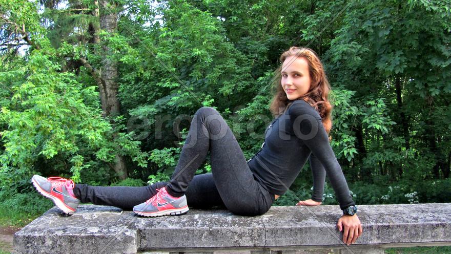 Девушка на каменной ограде в черном костюме.