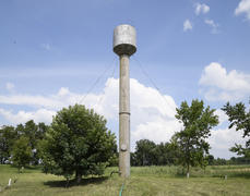 Серебряный водонапорная башня среди зеленой травы и деревьев