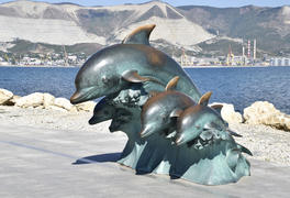 Бронзовая скульптура три дельфина на пляже.