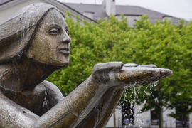 Статуя коленопреклоненной женщины в фонтане. Вода, стекающая с руки статуи.