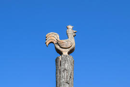 Фигурка петуха на пне дерева на фоне голубого неба