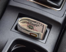 Несколько купюр американских долларов лежат в нише центральной консоли автомобиля