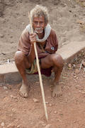Rustic old man sitting on the ground with a stick in his hands